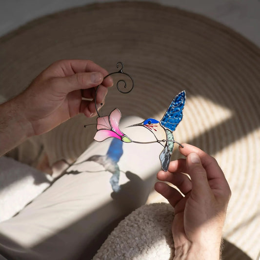 Hand holding a stained glass hummingbird and flower suncatcher, casting colorful shadow