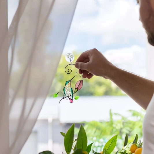 Man hanging a decorative stained glass hummingbird suncatcher in elegant green tones on a window
