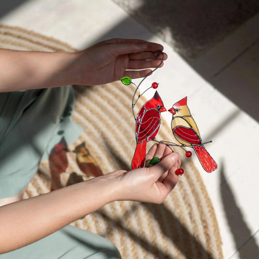 Stained glass cardinals suncatcher held by a person against a textured cover on the floor