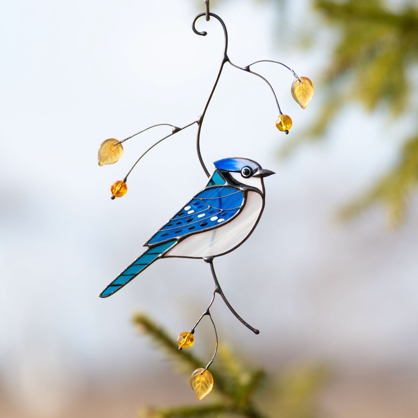 Stained glass blue jay suncatcher hanging among tree with yellow decorative beads