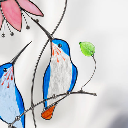 Close-up of a blue stained glass bird with orange tail and green leaf on wire branch.