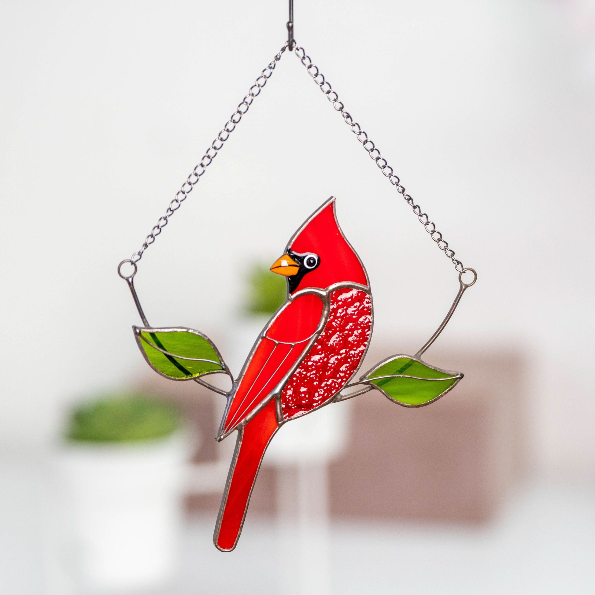 Close-up of stained glass cardinal in bright red color with chain and green leaves