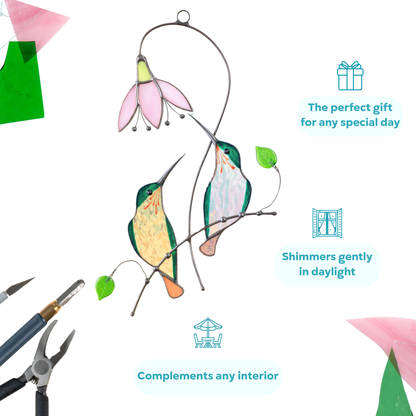 Green hummingbirds under a pink flower, surrounded by tools and glass pieces.
