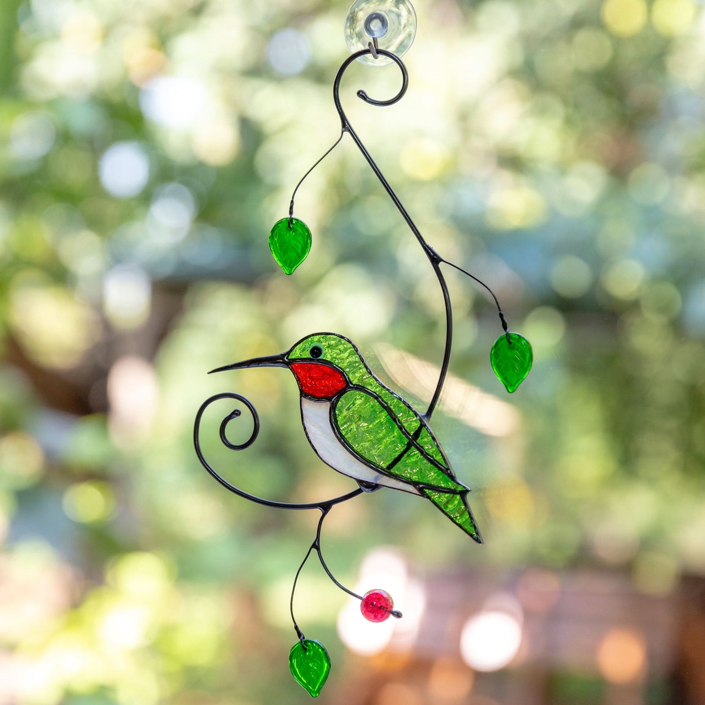 Bright green glass hummingbird with red throat hanging on a window outdoors