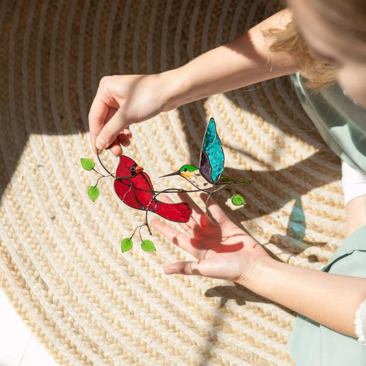 Person holding a colorful stained glass bird suncatcher, casting bright shadow on a woven surface