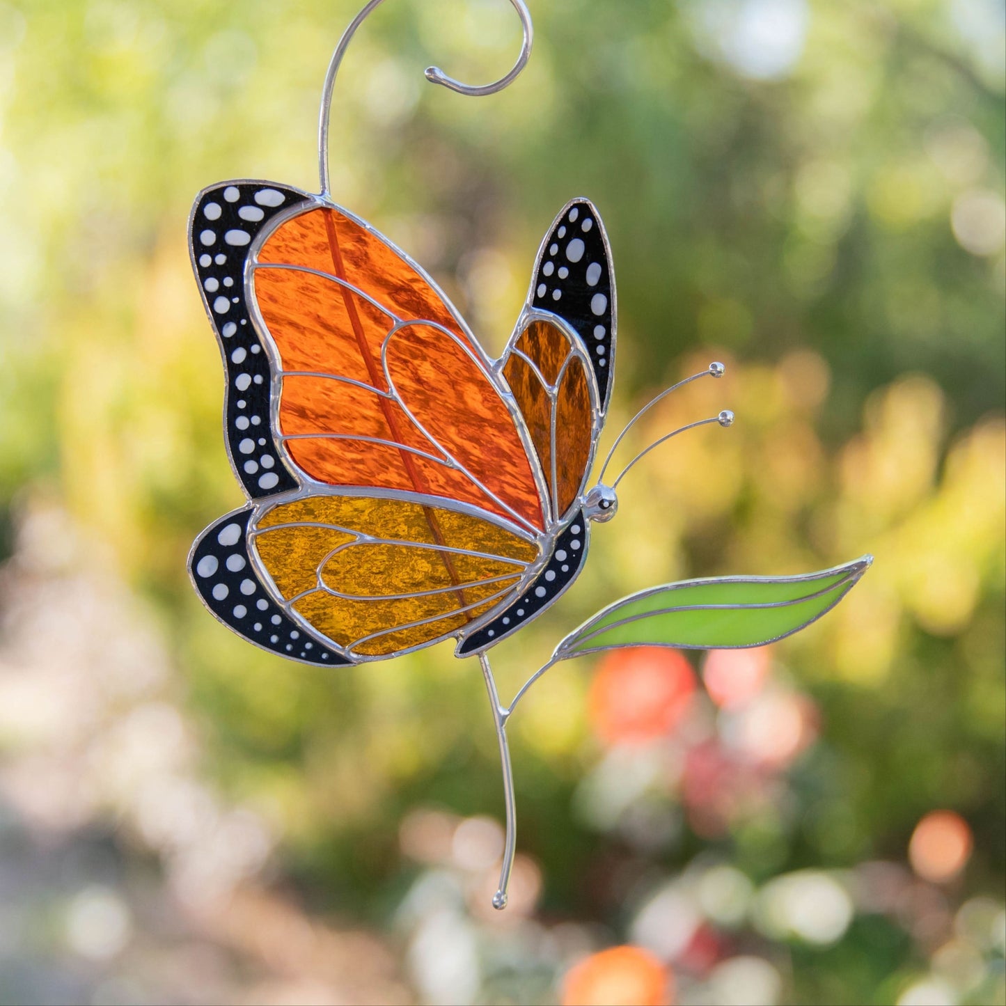 Side view stained glass monarch butterfly hanging outdoors with colorful background.