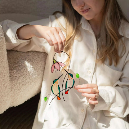 Girl holding a colorful stained glass hummmingbird pair suncatcher with floral design