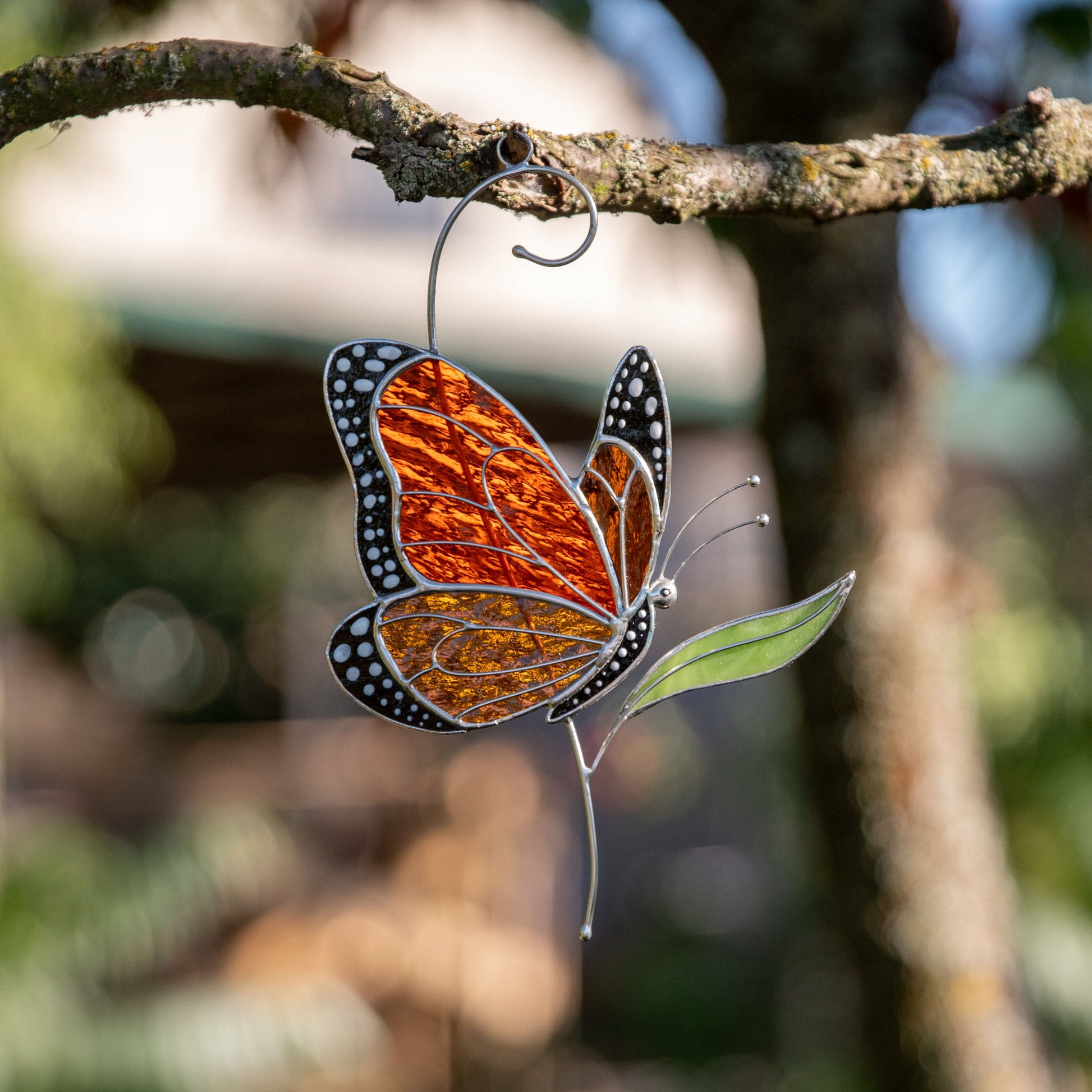 Orange stained glass monarch butterfly side view glowing beautifully in the garden sunlight.