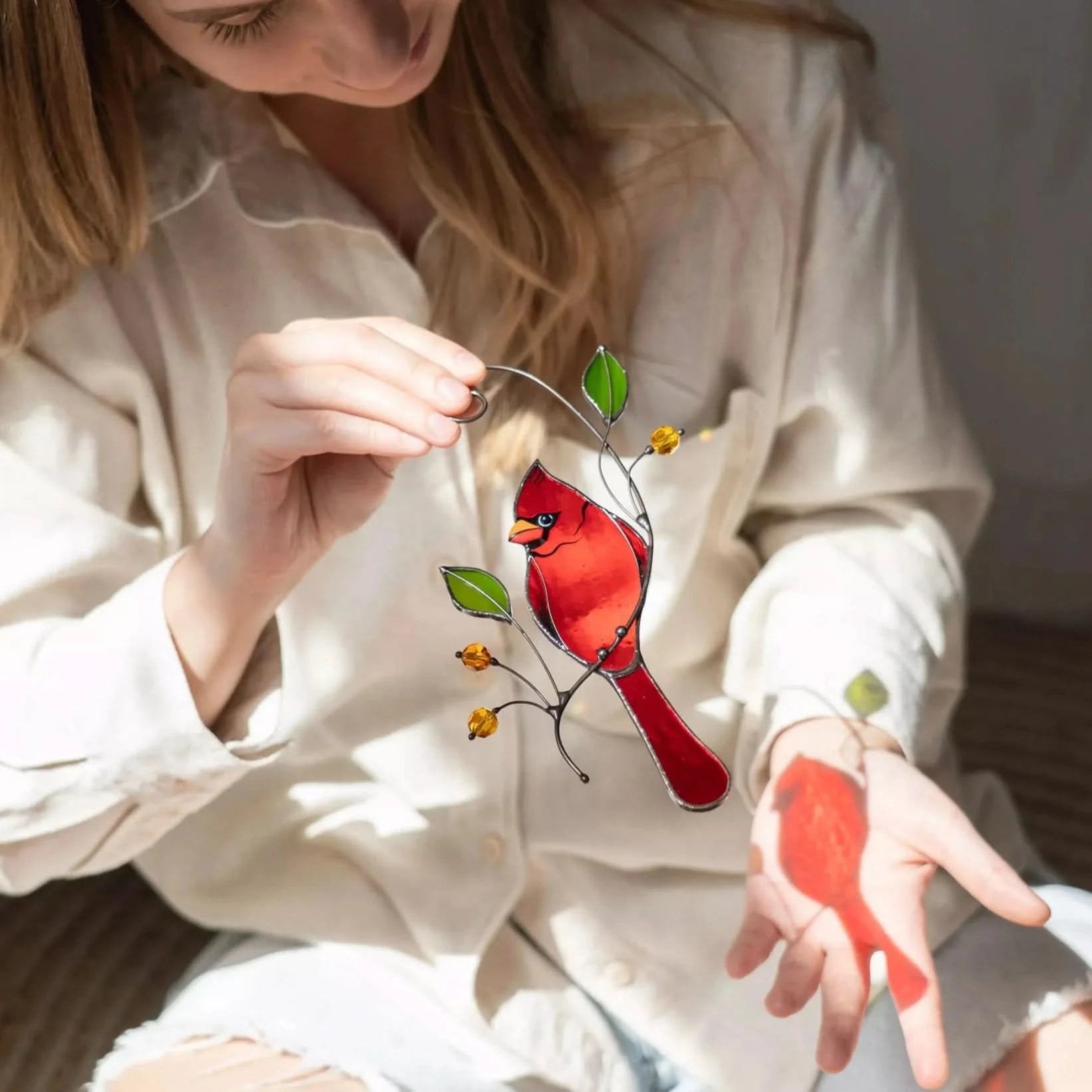 Woman holding a red cardinal stained glass bird suncatcher with a blurred background