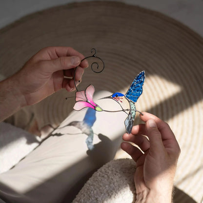 Hand holding a stained glass hummingbird and flower suncatcher, casting colorful shadow 