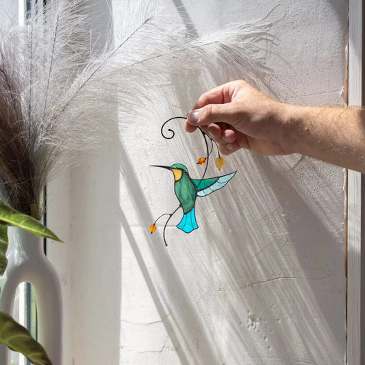 Hand holding a stained glass turquiose hummingbird suncatcher against a white wall with shadows