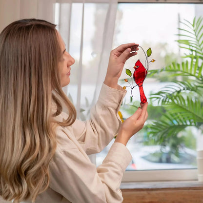 Woman holding a red stained glass cardinal in front of a window with plants outside