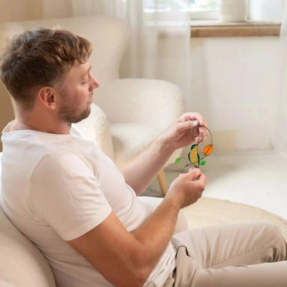 Man sitting on a couch holding stained glass hummingbird suncatcher in a bright living room.