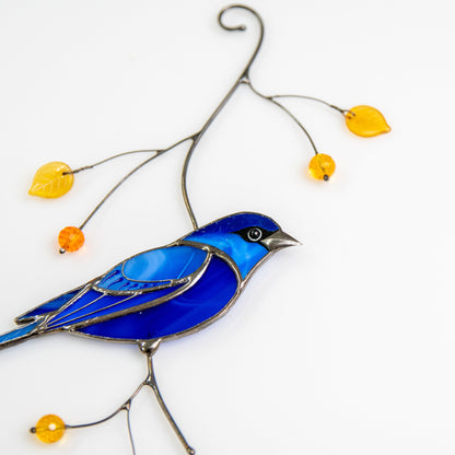 Close-up of a stained glass indigo bunting bird suncatcher with yellow beads, lying flat
