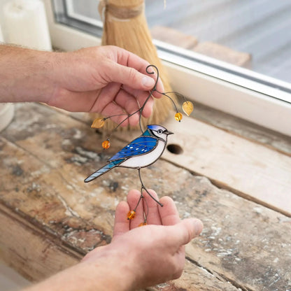 Stained glass blue jay suncatcher held by a hand on a wooden surface.