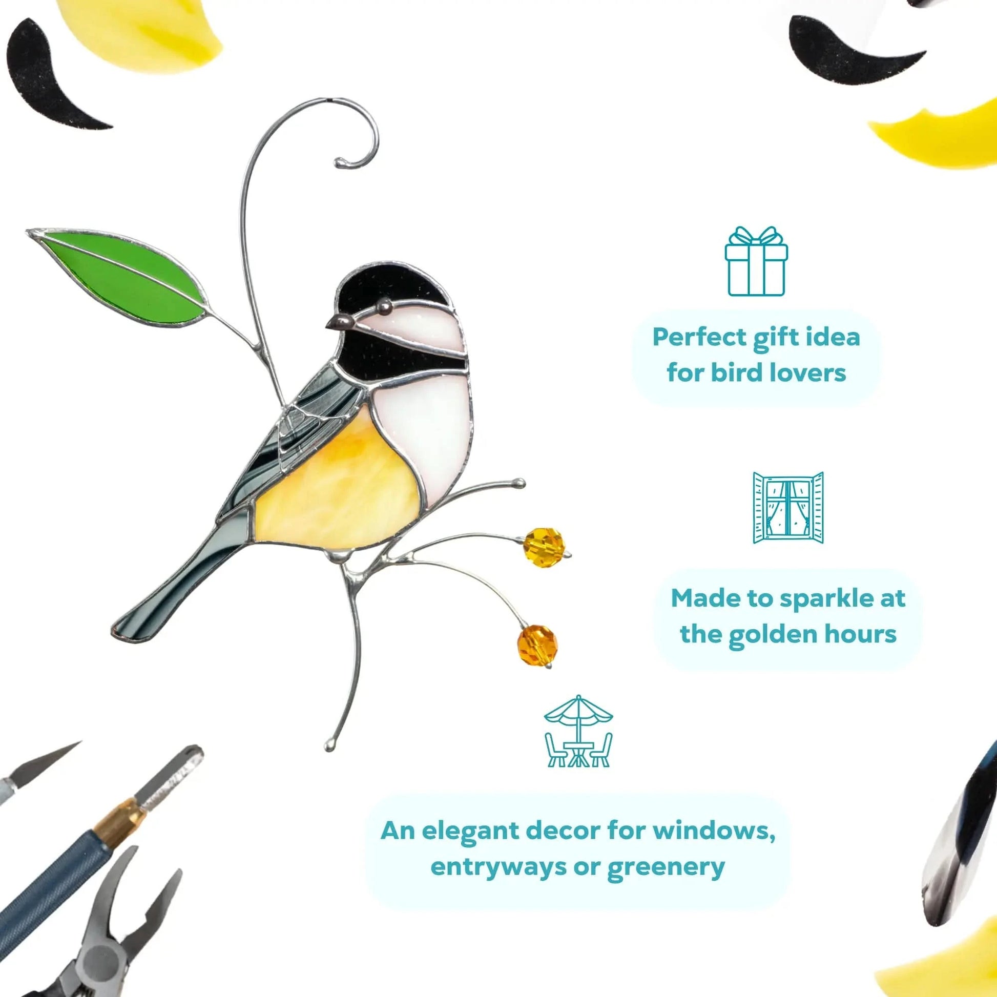 Chickadee suncatcher with yellow body, black and white head, amber beads and green leaf, hanging near tools on white background.