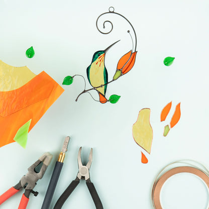 Glass cutting tools and stained glass pieces laid out around finished hummingbird and orange flower