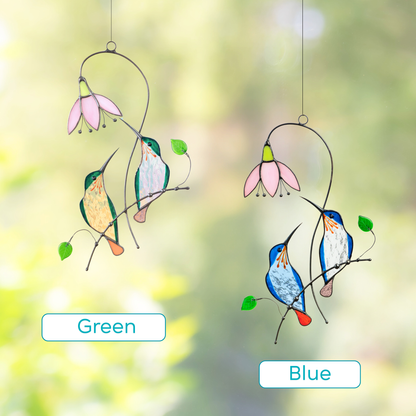 Two stained glass suncatchers featuring hummingbird pairs in green and blue, each near a pink flower.