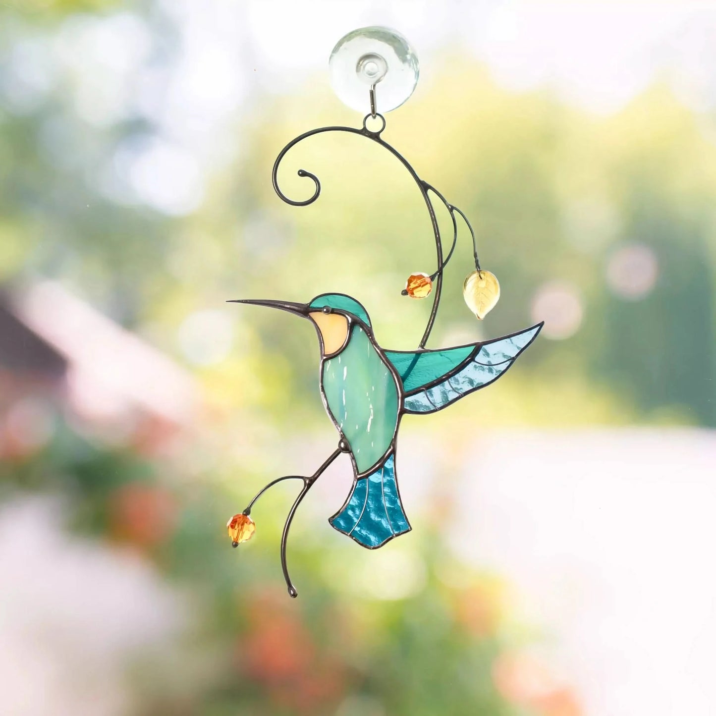 Stained glass blue hummingbird window hanging with a blurred garden background